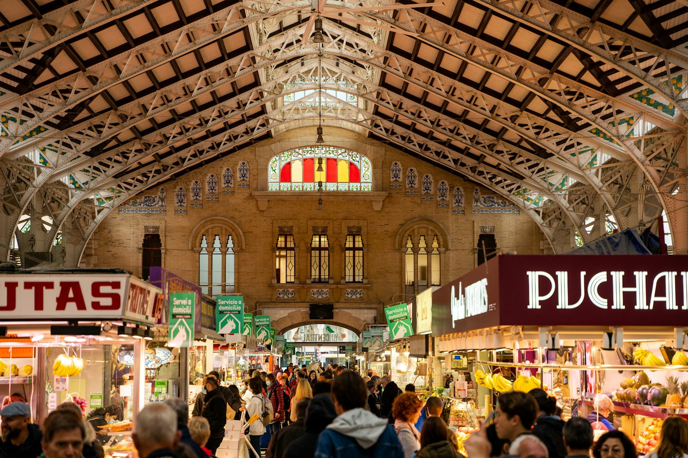 Ihmisiä ostoksilla Valencian Mercado Centralin katetussa hallissa koristeellisen katon ja ruokakojujen alla